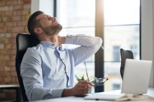 Male office manager closing eyes and touching his neck while feeling pain after sitting too long